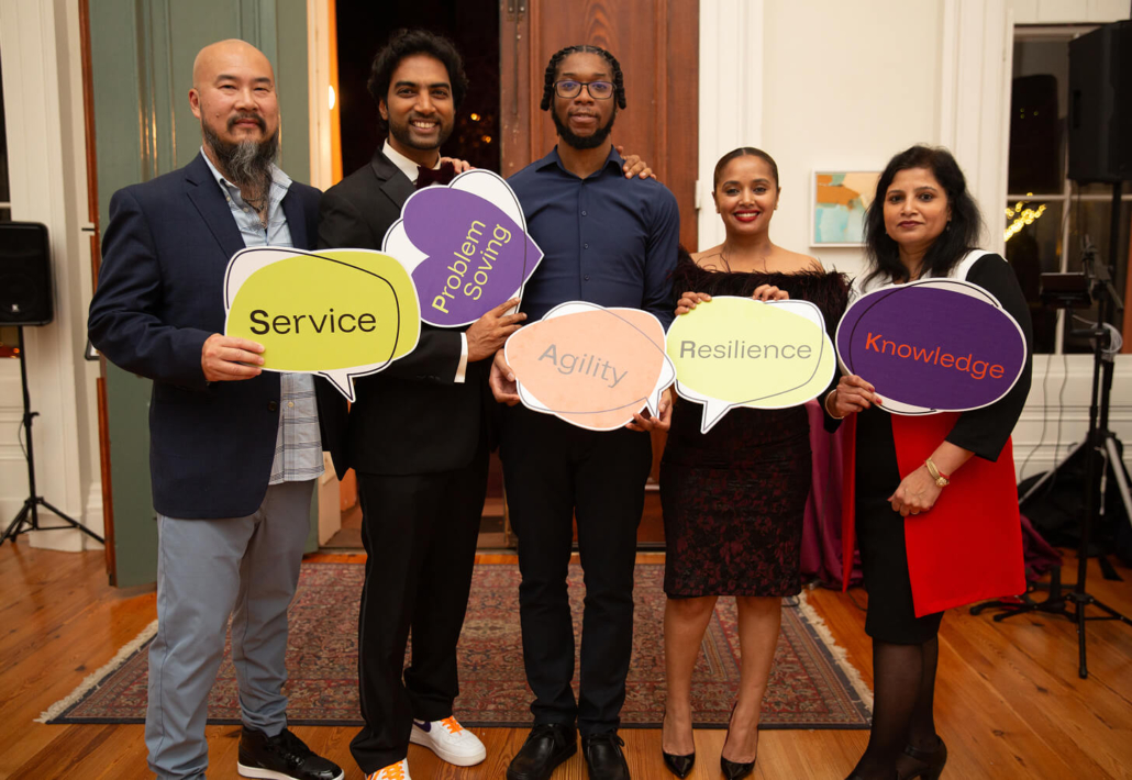 Group of diverse people holding signs with words like "Service," "Problem Solving," "Agility," "Resilience," and "Knowledge"