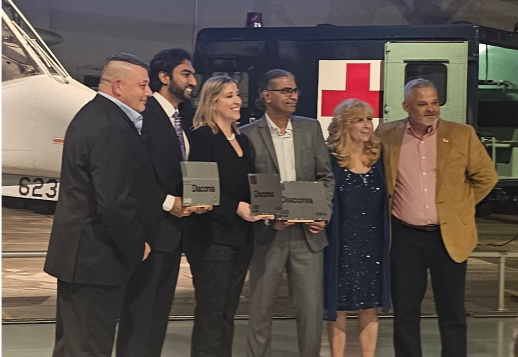 Six people stand together holding awards in front of a helicopter with a Red Cross symbol.