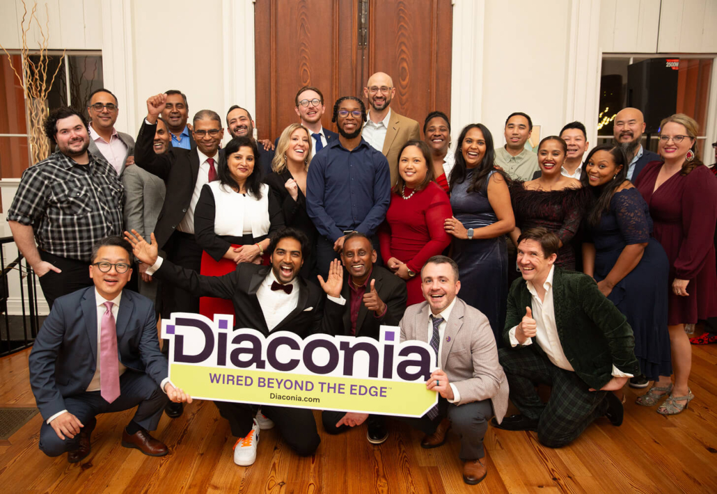 A diverse group of people celebrating at a holiday gathering, holding a Diaconia sign and smiling cheerfully.