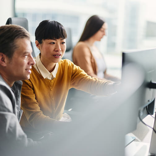 Three diverse professionals collaborate at computers in a modern office, analyzing data related to AI decision support tools.