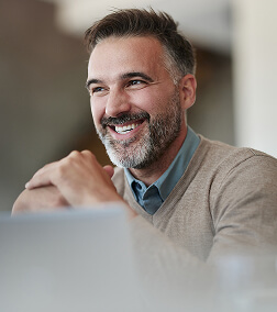 Diaconia Applied R and D PreFooter A smiling man with a beard and gray hair works on a laptop in a professional setting.