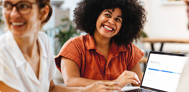 A smiling woman with curly hair interacts with a laptop, emphasizing human-centered AI in a collaborative setting.