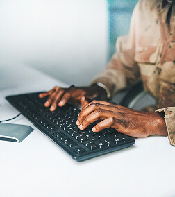 A person typing on a black keyboard at a white desk with a blurred background.
