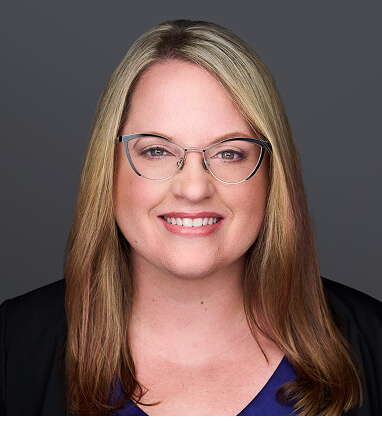 Breanna Wheeler, a woman with long blonde hair and glasses, smiles in a professional headshot against a gray background.
