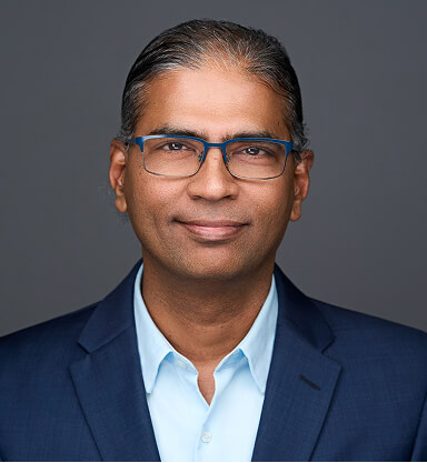 A professional headshot of Srikanth Swaminathan wearing glasses, a navy blazer, and a light blue shirt against a gray
