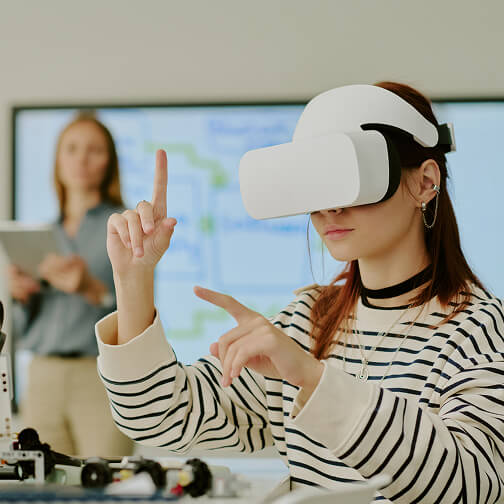 A woman wearing a virtual reality headset interacts with a virtual environment, with another person blurred in the
