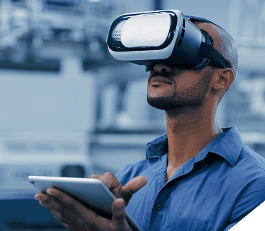 A man wearing a virtual reality headset and holding a tablet in an industrial or office environment.