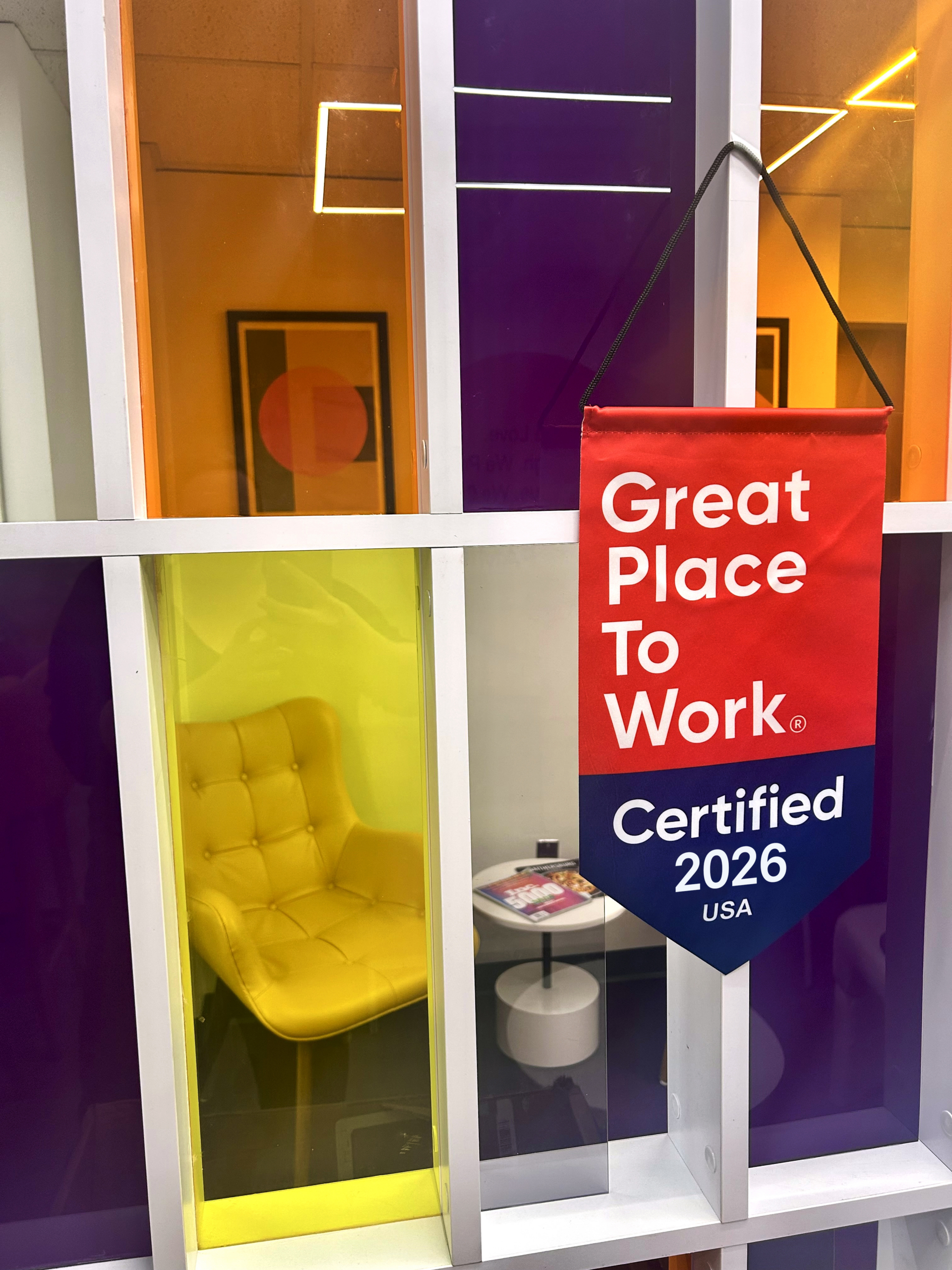 A yellow chair with a tufted backrest is positioned inside a colorful display booth with purple, orange, and yellow panels,