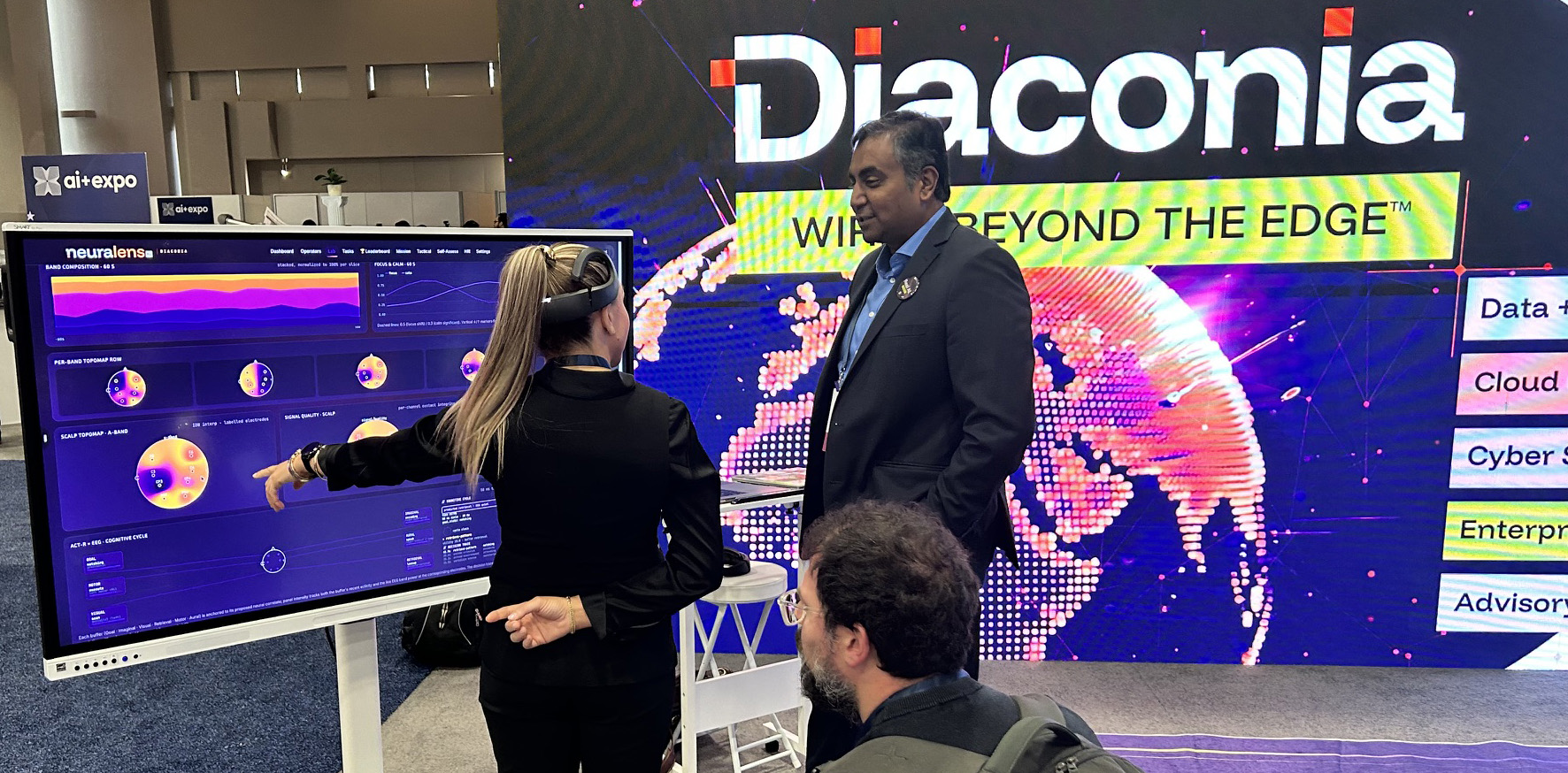 A woman wearing a virtual reality headset asks questions about NeuraLens XL's data visualizations to the data engineer at a technology expo booth.
