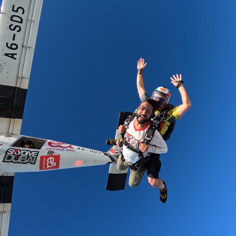 Praveen skydiving with a wide smile, free-falling from a plane against a clear blue sky.